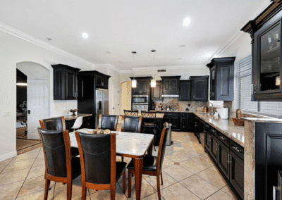 Modern kitchen with black cabinets, stainless steel appliances, a central dining table with six chairs, granite countertops, and tiled floors.