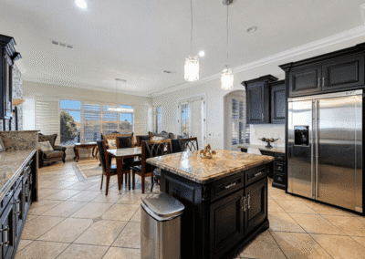 Spacious kitchen with dark cabinets, granite countertops, stainless steel appliances, tile flooring, and an adjacent dining and living area with large windows.