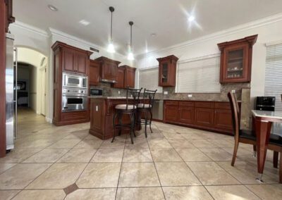 Spacious kitchen with brown wooden cabinets, granite countertops, stainless steel appliances, tile floor, and a central island with high chairs.